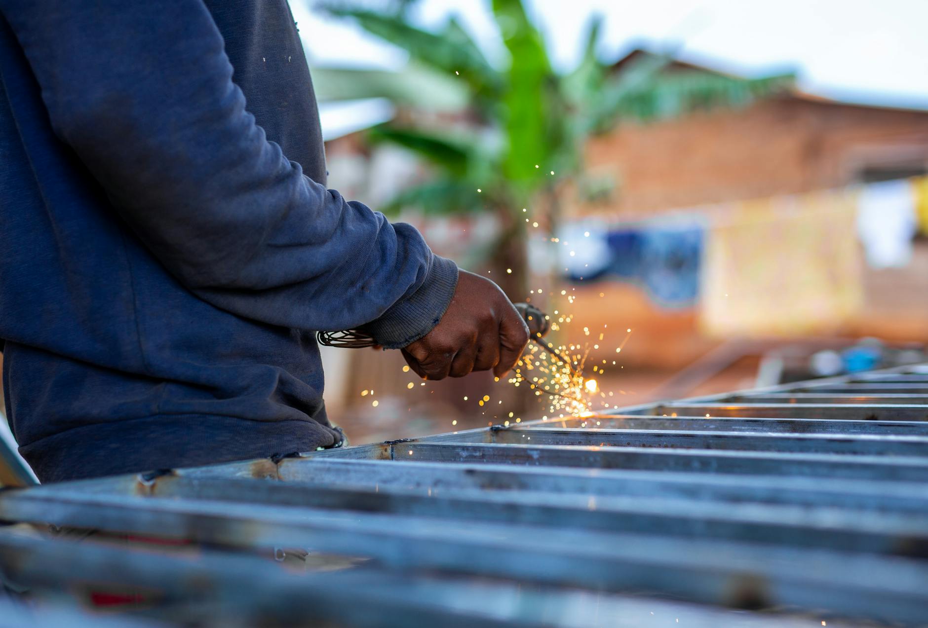 A person welding metal outdoors, creating bright sparks against a blurred background.